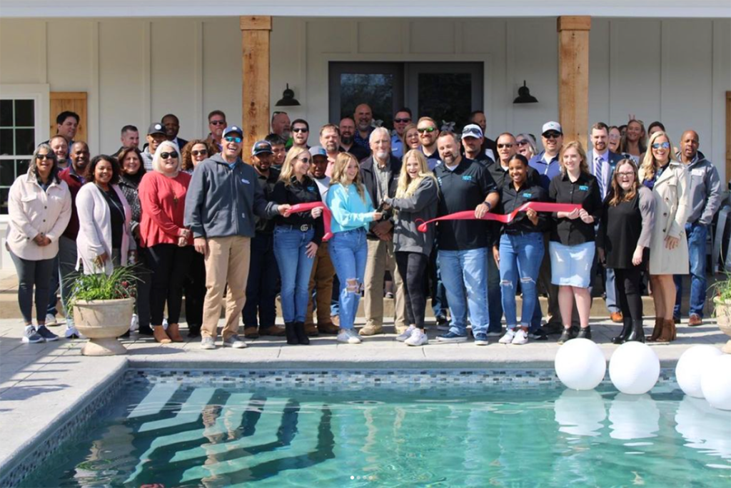 Pool opening day celebration, group of happy people cutting ribbon next to swimming pool